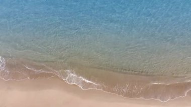 Tropikal kumsal dalgalarının kumsala ulaşan deniz dalgalarının drone görüntüsü kumlu sahil şeridinde mavi okyanus suyuyla buluşuyor..