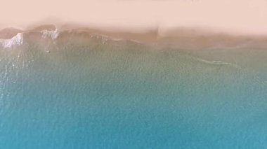 Tropikal kumsal dalgalarının kumsala ulaşan deniz dalgalarının drone görüntüsü kumlu sahil şeridinde mavi okyanus suyuyla buluşuyor..