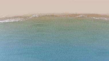 Tropikal kumsal dalgalarının kumsala ulaşan deniz dalgalarının drone görüntüsü kumlu sahil şeridinde mavi okyanus suyuyla buluşuyor..