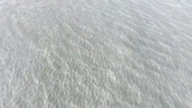 Kristal berrak tropik sahil sularının hava aracı görüntüsü dalgalanmalar ve su yansımaları sergiliyor.