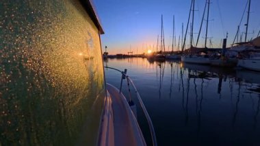 Tekne yan penceresinde çiğ taneleri marina rıhtımında güneşin doğuşunda ıslanıyor.