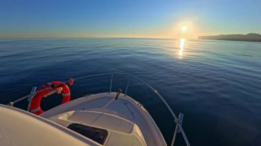 Bir yat, gün batımının ılık parıltısının altında derin mavi denizde süzülür.