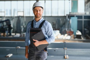 Erkek fabrika tamircileri veya güvenlik üniformalı mühendisler endüstriyel üretim hatlarında metal sondaj makineleri, çelik işleme endüstrisi ve mekanik bakım üzerinde çalışıyorlar.