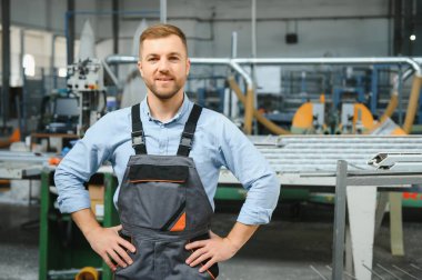 Üniformalı fabrika işçisinin portresi üretim hattında endüstriyel makinenin yanında duruyor. Endüstride çalışan insanlar.