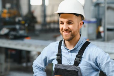 Üniformalı fabrika işçisinin portresi üretim hattında endüstriyel makinenin yanında duruyor. Endüstride çalışan insanlar.