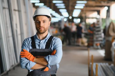 Üniformalı fabrika işçisinin portresi üretim hattında endüstriyel makinenin yanında duruyor. Endüstride çalışan insanlar.