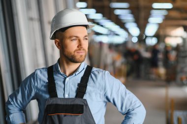 Üniformalı fabrika işçisinin portresi üretim hattında endüstriyel makinenin yanında duruyor. Endüstride çalışan insanlar.