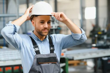 Üniformalı fabrika işçisinin portresi üretim hattında endüstriyel makinenin yanında duruyor. Endüstride çalışan insanlar.