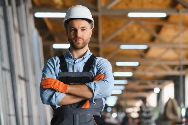 Üniformalı fabrika işçisinin portresi üretim hattında endüstriyel makinenin yanında duruyor. Endüstride çalışan insanlar.