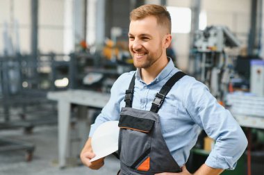 Üniformalı fabrika işçisinin portresi üretim hattında endüstriyel makinenin yanında duruyor. Endüstride çalışan insanlar.