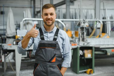 Üniformalı fabrika işçisinin portresi üretim hattında endüstriyel makinenin yanında duruyor. Endüstride çalışan insanlar.