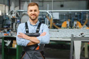 Üniformalı fabrika işçisinin portresi üretim hattında endüstriyel makinenin yanında duruyor. Endüstride çalışan insanlar.