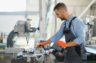 Erkek fabrika tamircileri veya güvenlik üniformalı mühendisler endüstriyel üretim hatlarında metal sondaj makineleri, çelik işleme endüstrisi ve mekanik bakım üzerinde çalışıyorlar.