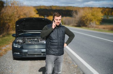 Adamın biri tamirciyle konuşmak için telefon numarasını arıyor. Araba yol kenarında arıza yaptı. Tamir, yardım, sorun, onarım kavramı. Bulanık arkaplan