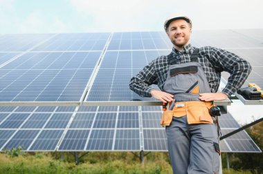 Çatıda elinde güneş panelleriyle kameraya gülümseyen bir tamirci.