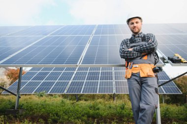 Çatıda elinde güneş panelleriyle kameraya gülümseyen bir tamirci.