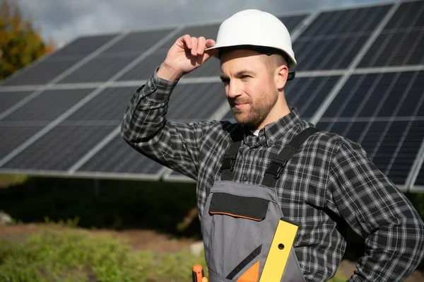 Male worker in uniform outdoors with solar batteries at sunny day