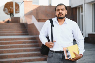 Üniversite kampüsündeki merdivenlerde oturan mutlu Hintli öğrenci.