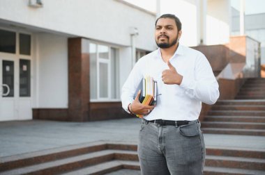 Sırt çantalı Hintli öğrenci güneşli bir günde kitap tutuyor..