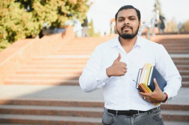 Sırt çantalı Hintli öğrenci güneşli bir günde kitap tutuyor..