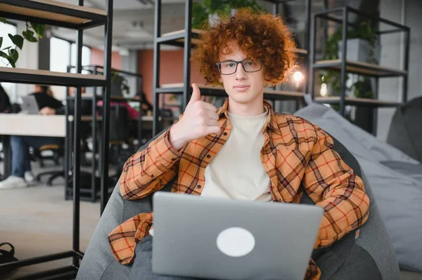 stock image Young happy male freelancer in casual clothes with toothy smile looking at camera sitting in cafe with laptop and using mobile phone