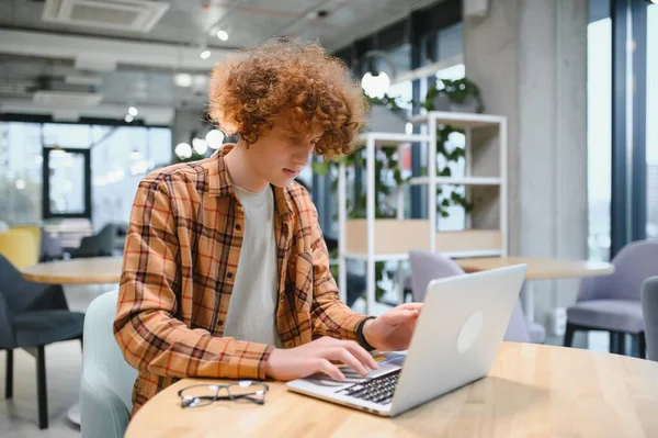 stock image Portrait of Caucasian male freelancer in trendy apparel sitting at cafeteria table and doing remote work for programming design of public website, skilled software developer posing in coworking space