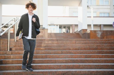 University.Smiling genç öğrenci adam bir kitap ve bir çanta Üniversitesi arka plan üzerinde tutarak. Genç gülümseyen öğrenci açık havada yaşam tarzı. City.Student