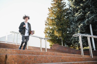 Mutlu yakışıklı üniversite, üniversite öğrencisi ya da başarılı genç bir öğrenci. Gün batımında kitap okuyan ve gülümseyen bir öğrenci. Boşluğu kopyala.
