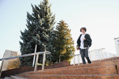 Çanta ile kampüste duran bir mutlu erkek öğrenci portresi.