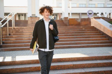 Mutlu yakışıklı üniversite, üniversite öğrencisi ya da başarılı genç bir öğrenci. Gün batımında kitap okuyan ve gülümseyen bir öğrenci. Boşluğu kopyala.