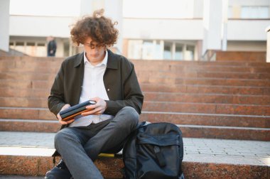 Mutlu genç öğrenci, güneşli bir günde, kitap okuyor ve çok gülümsüyor..