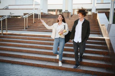 Öğrenci çift dışarıda konuşuyor, ellerinde kitaplar, notlar ve diğer öğrenme materyalleri var..