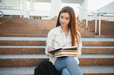 Sırt çantası ve defterleriyle ayakta duran ve gülümseyen neşeli çekici genç kadın.