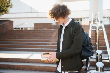 Mutlu genç öğrenci, güneşli bir günde, kitap okuyor ve çok gülümsüyor..