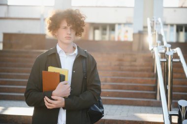 Çanta ile kampüste duran bir mutlu erkek öğrenci portresi.