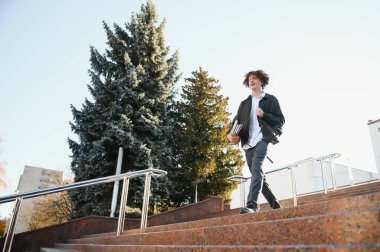 University.Smiling genç öğrenci adam bir kitap ve bir çanta Üniversitesi arka plan üzerinde tutarak. Genç gülümseyen öğrenci açık havada yaşam tarzı. City.Student