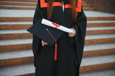 Mutlu tatlı esmer beyaz kız gülümsüyor. Siyah bir havan tahtasının içinde, kırmızı püsküllü, cüppeli, kahverengi kıvırcık saçlı, diplomalı.