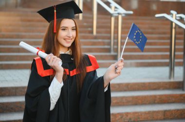 Mutlu tatlı esmer beyaz kız gülümsüyor. Siyah bir havan tahtasının içinde, kırmızı püsküllü, cüppeli, kahverengi kıvırcık saçlı, diplomalı.
