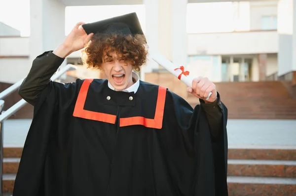 stock image excited graduate student in gown with risen hands holding diploma