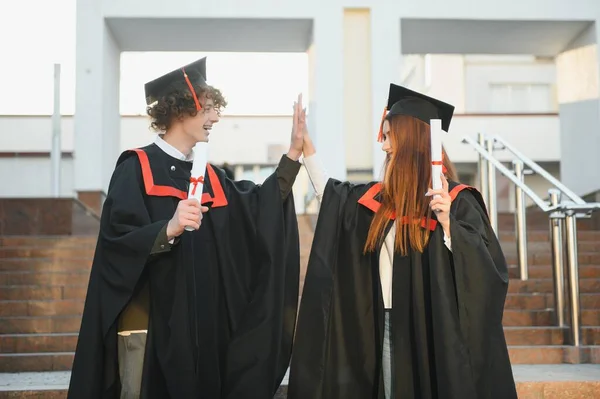 两个穿着黑色校服和帽子的快乐的学生站在书架上的图书馆里 教育概念 现代一代 — 图库照片