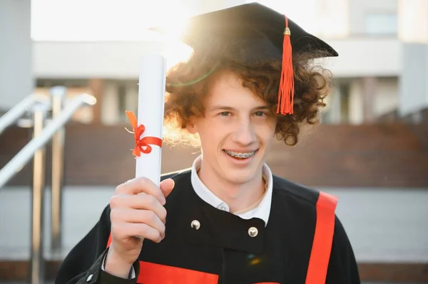 Szczęśliwy Uśmiechnięty Absolwent Uniwersytetu Płaszczu Trzymając Dyplom Ręce Wyrażając Szczęście — Zdjęcie stockowe