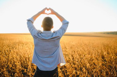 Adam sahanın ortasında tek başına duruyor. Eller yukarı ve parmaklar kalp şeklinde. Yaz sonu ya da sonbahar başında hasat zamanı. Çiftçi tarım uzmanı.