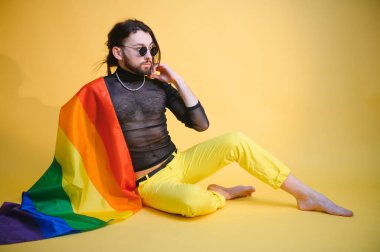 Beyaz arka planda LGBT Rainbow bayrağı taşıyan gururlu, yakışıklı genç bir adam. Eşcinsel gurur bayrağı taşıyan adam