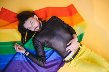 Beyaz arka planda LGBT Rainbow bayrağı taşıyan gururlu, yakışıklı genç bir adam. Eşcinsel gurur bayrağı taşıyan adam