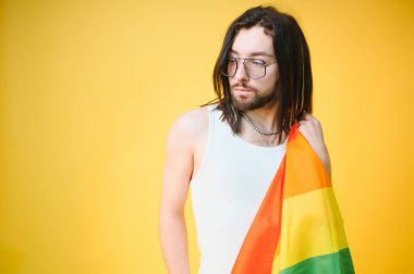 Beyaz arka planda LGBT Rainbow bayrağı taşıyan gururlu, yakışıklı genç bir adam. Eşcinsel gurur bayrağı taşıyan adam