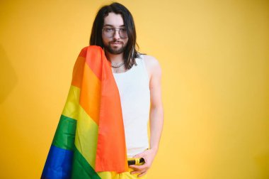 Eşcinsel adam renkli arka plan stüdyo resminde izole edilmiş gökkuşağı çizgili bayrak tutuyor. Insanlar yaşam tarzı lgbtq konsepti.