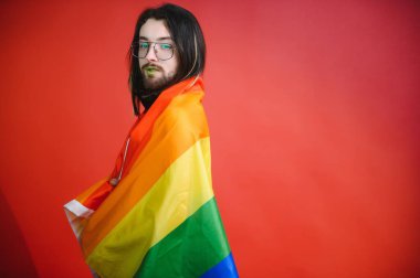 Beyaz arka planda LGBT Rainbow bayrağı taşıyan gururlu, yakışıklı genç bir adam. Eşcinsel gurur bayrağı taşıyan adam