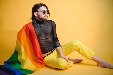 Beyaz arka planda LGBT Rainbow bayrağı taşıyan gururlu, yakışıklı genç bir adam. Eşcinsel gurur bayrağı taşıyan adam