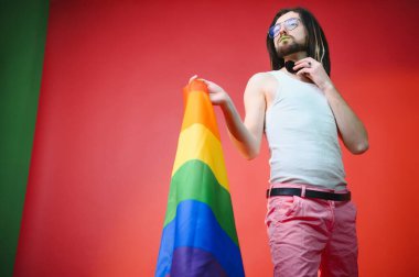Eşcinsel adam renkli arka plan stüdyo resminde izole edilmiş gökkuşağı çizgili bayrak tutuyor. Insanlar yaşam tarzı lgbtq konsepti.