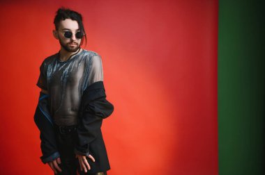 Genç eşcinsel adam stüdyoda duruyor ve kameraya poz veriyor.